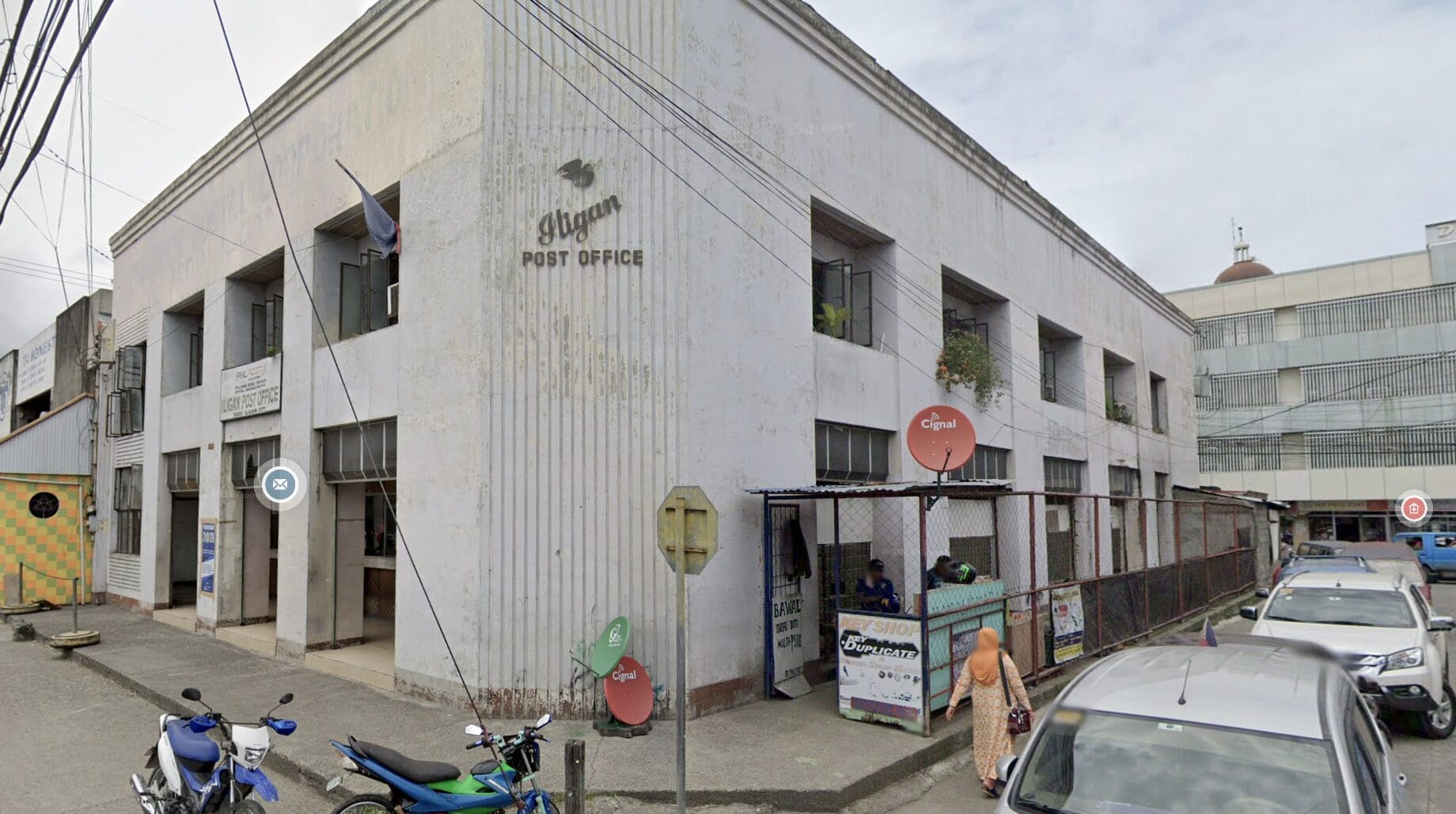 Baguio Post Office Building, Philippines, na may mga motorsiklo at kotse na nakaparada sa labas sa isang maulap na araw.